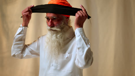 Fotografía-De-Estudio-De-Un-Hombre-Sikh-Mayor-Con-Barba-Atando-Tela-Para-Un-Turbante-Contra-Un-Fondo-Liso,-Filmada-En-Tiempo-Real